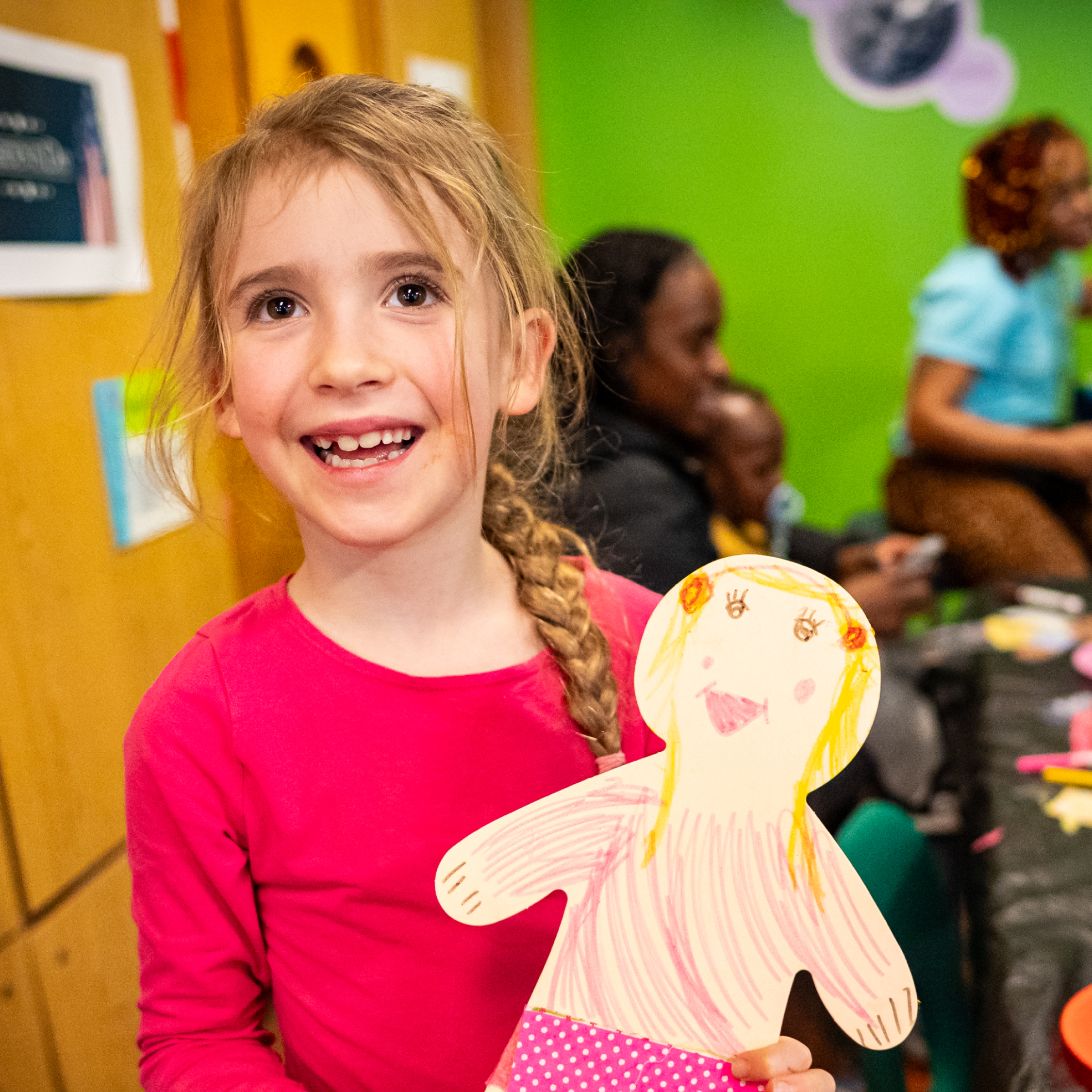 Child happily holds up a portrait they made.