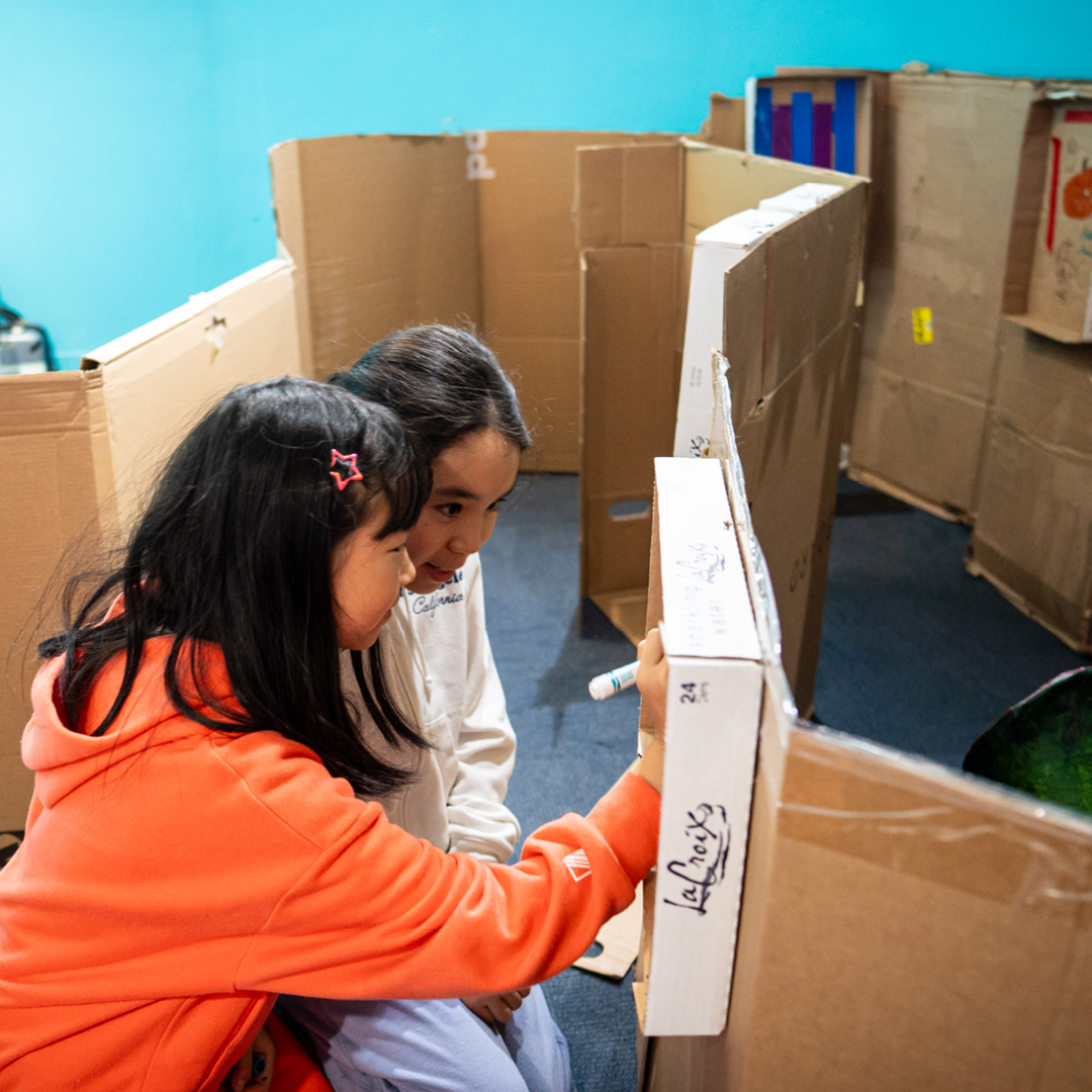 Two children work on an installation made out of cardboard