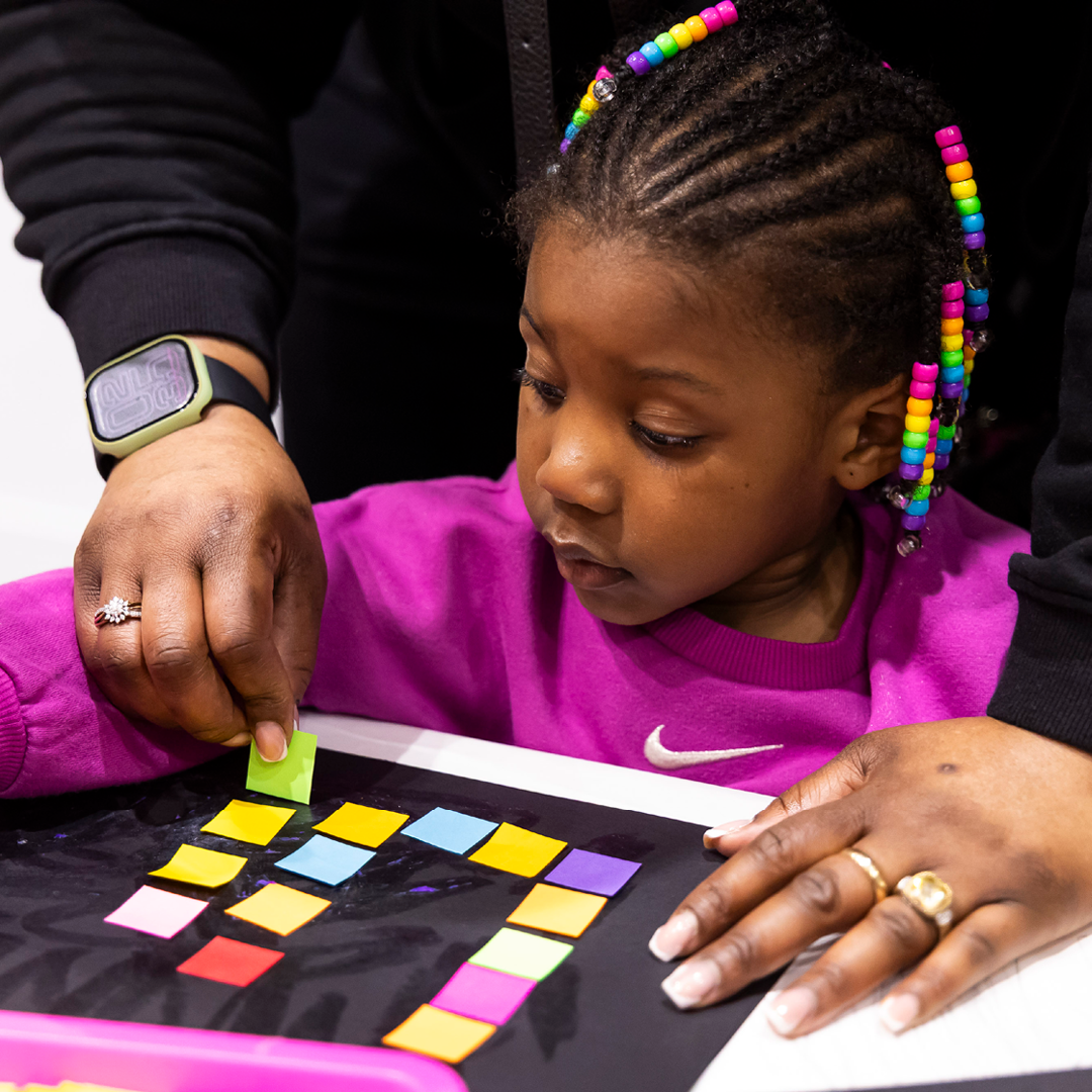 Child makes a collage using colorful tiles.
