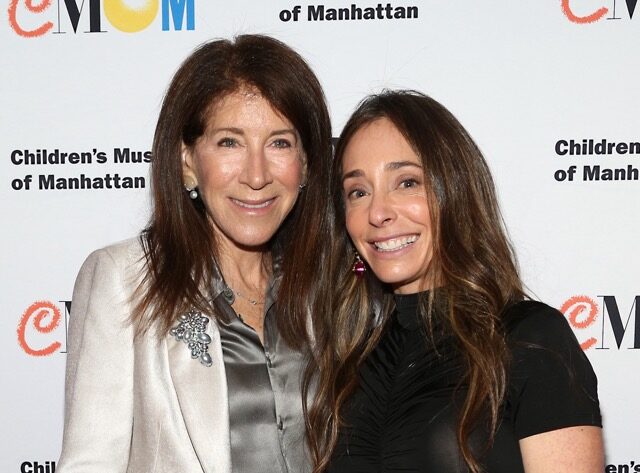 Two women smile at camera in front of Children's Museum of Manhattan Step &amp; Repeat