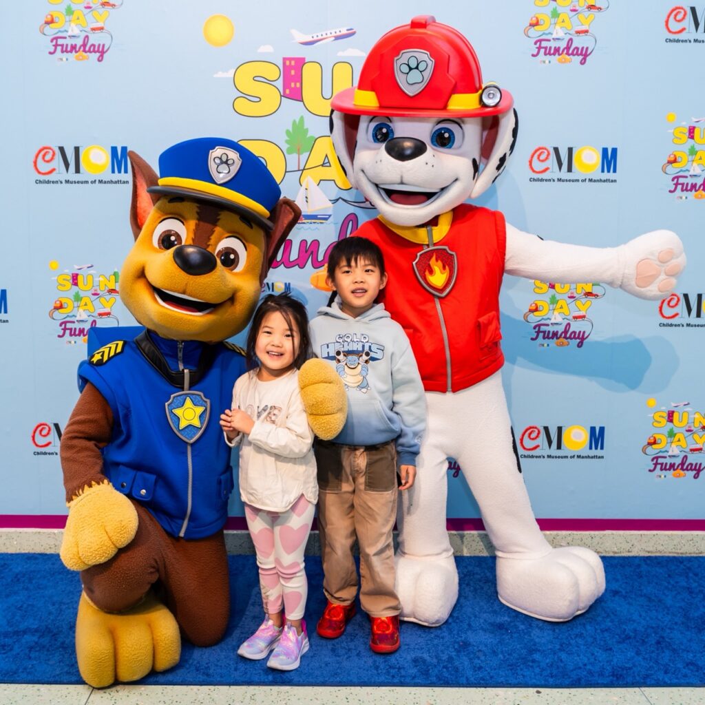 Two small children smile with two characters from Paw Patrol