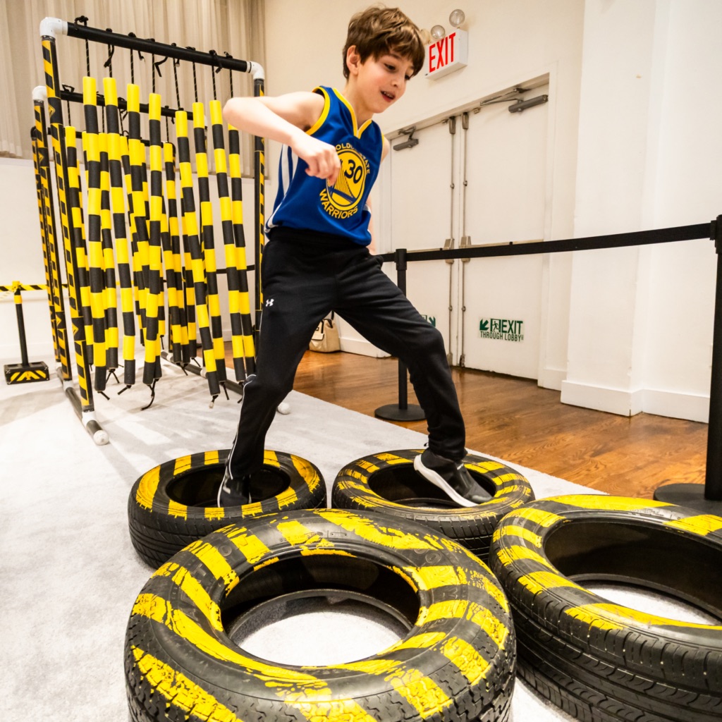A child plays on a child obstacle course, running through a series of tires.