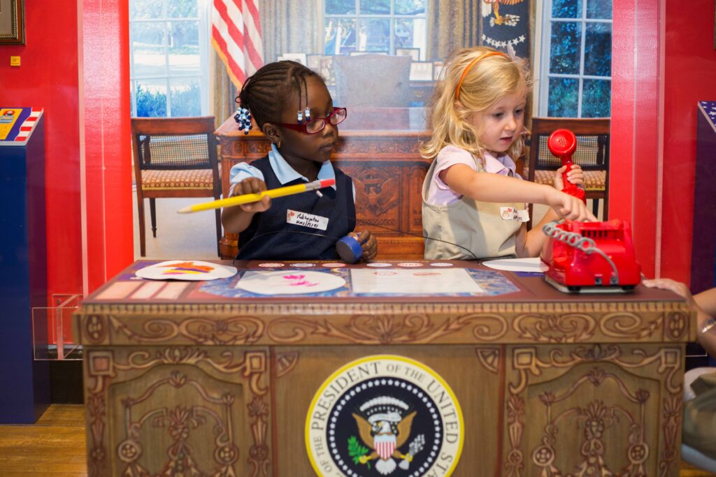 Two young children at a mock desk in a mock Oval Office