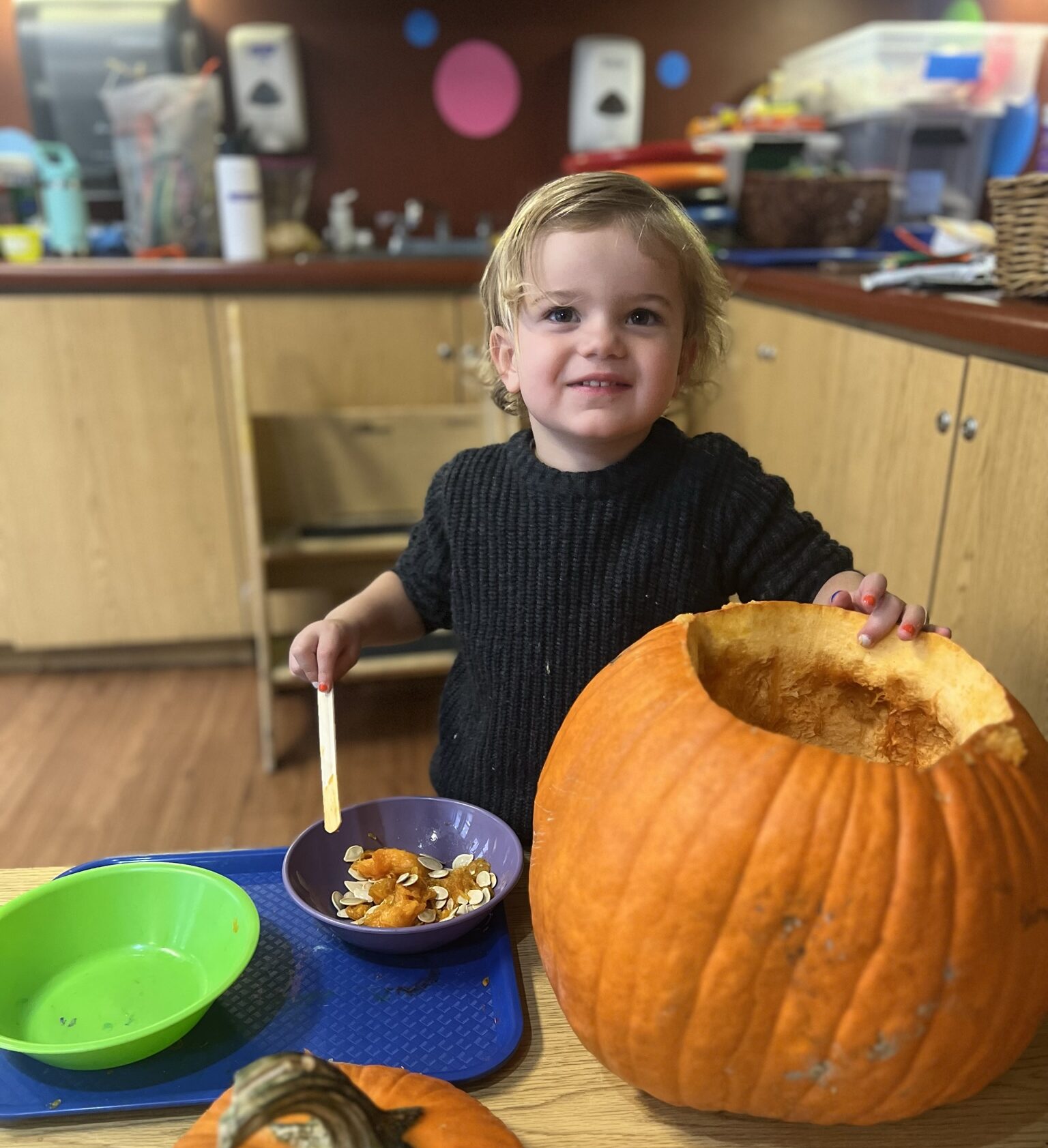 A young child smiles at the camera while decorating a pumpkin