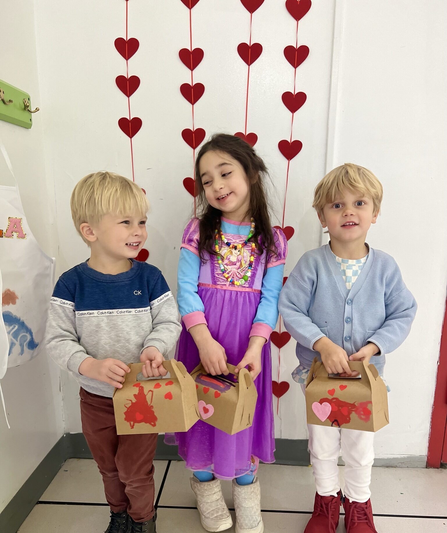 Three small children hold crafted boxes and smile at the camera