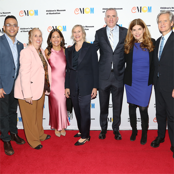 Seven adults smile at the camera in front of a step-and-repeat on a red carpet at a gala.