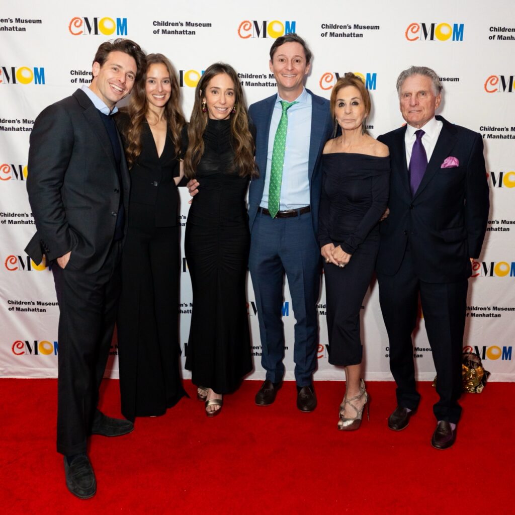 Six adults smile at the camera in front of a step-and-repeat on a red carpet at a gala.
