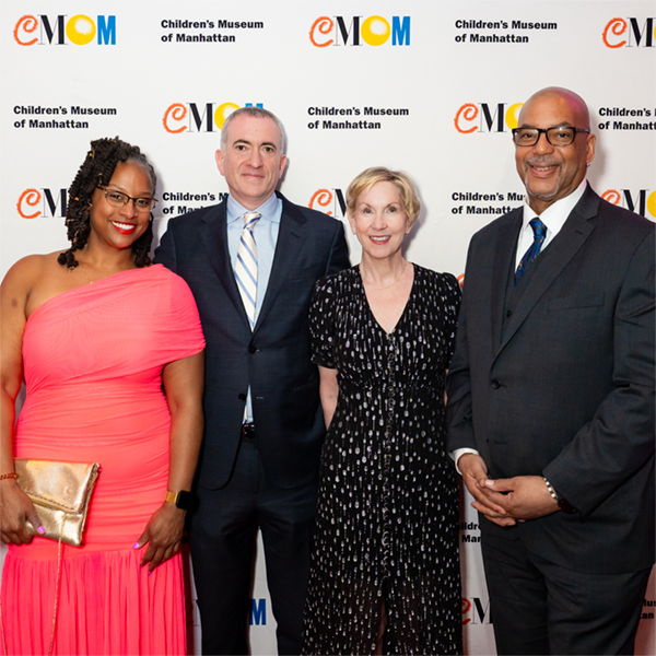 Four adults smile at the camera in front of a step-and-repeat on a red carpet at a gala.