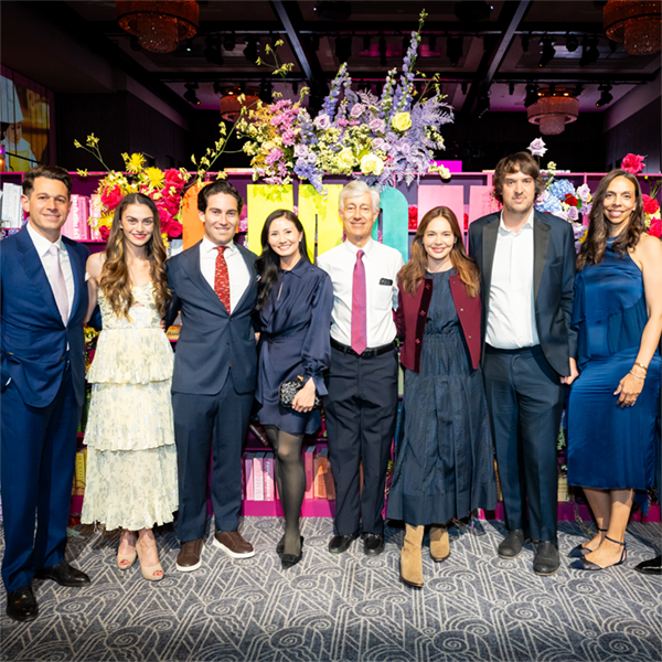 Eight adults smile at the camera in front of a floral photo opportunity spot at a gala.