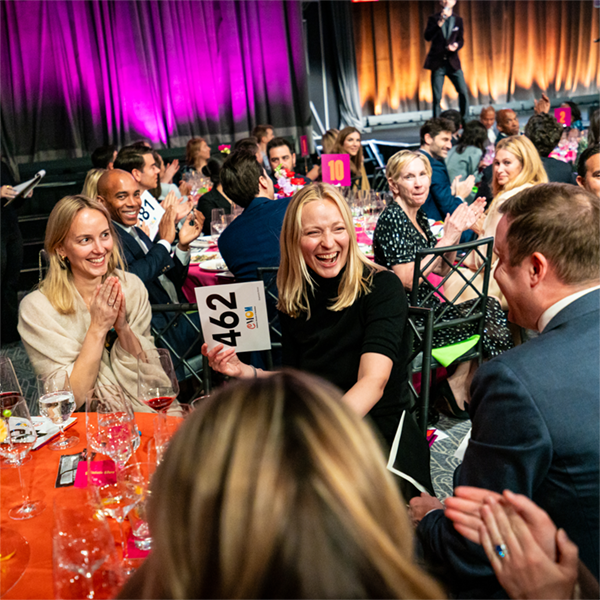 A candid photo of an auction prize winner with her numbered paddle, while onlookers applaud.