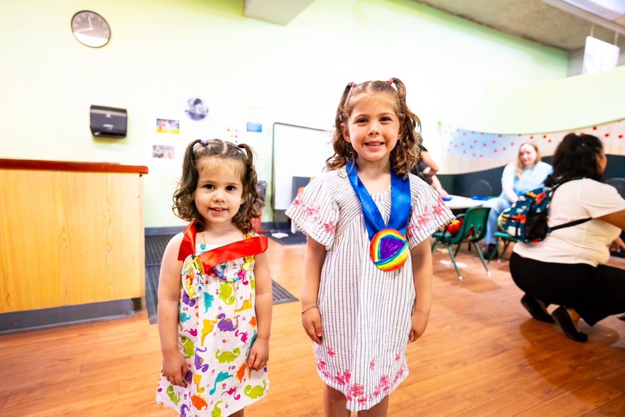 Two small children smile at the camera, wearing handmade crafted "medals"