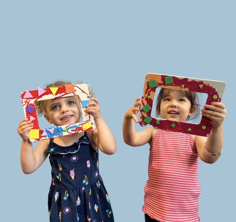 Two small children hold up colorful crafted frames in front of their faces
