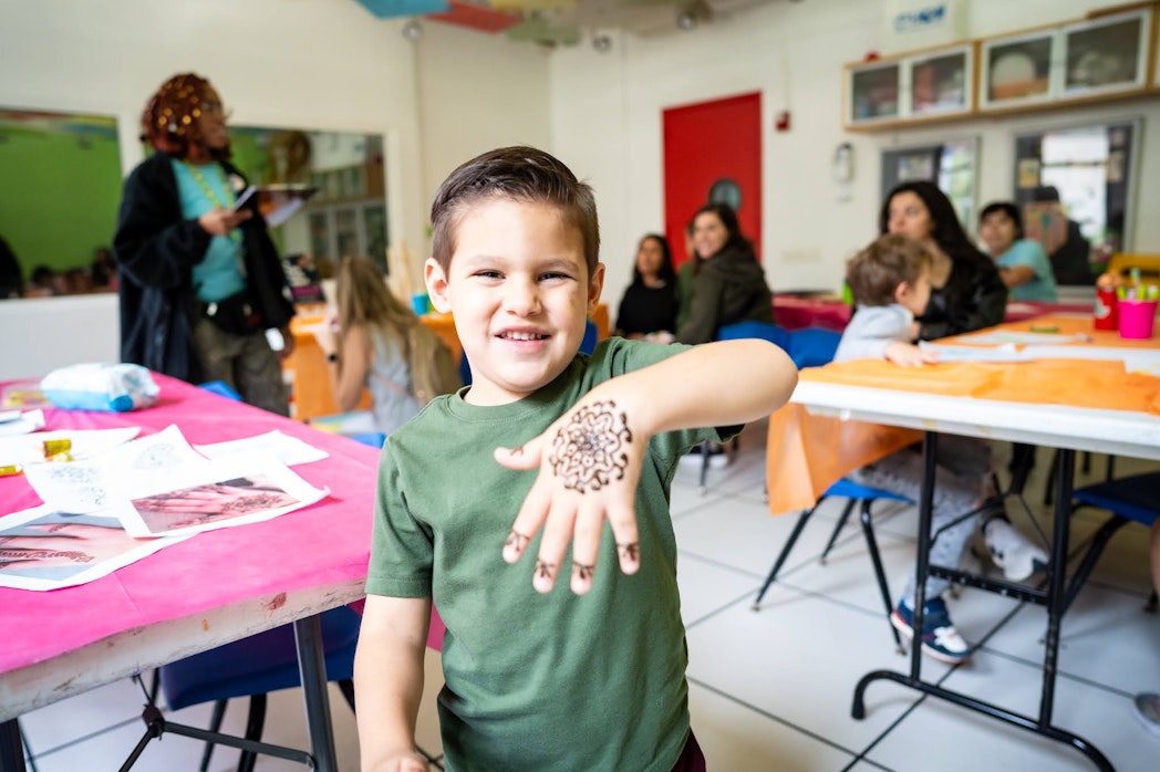 A child smiles at the camera and shows off painted henna on his hand